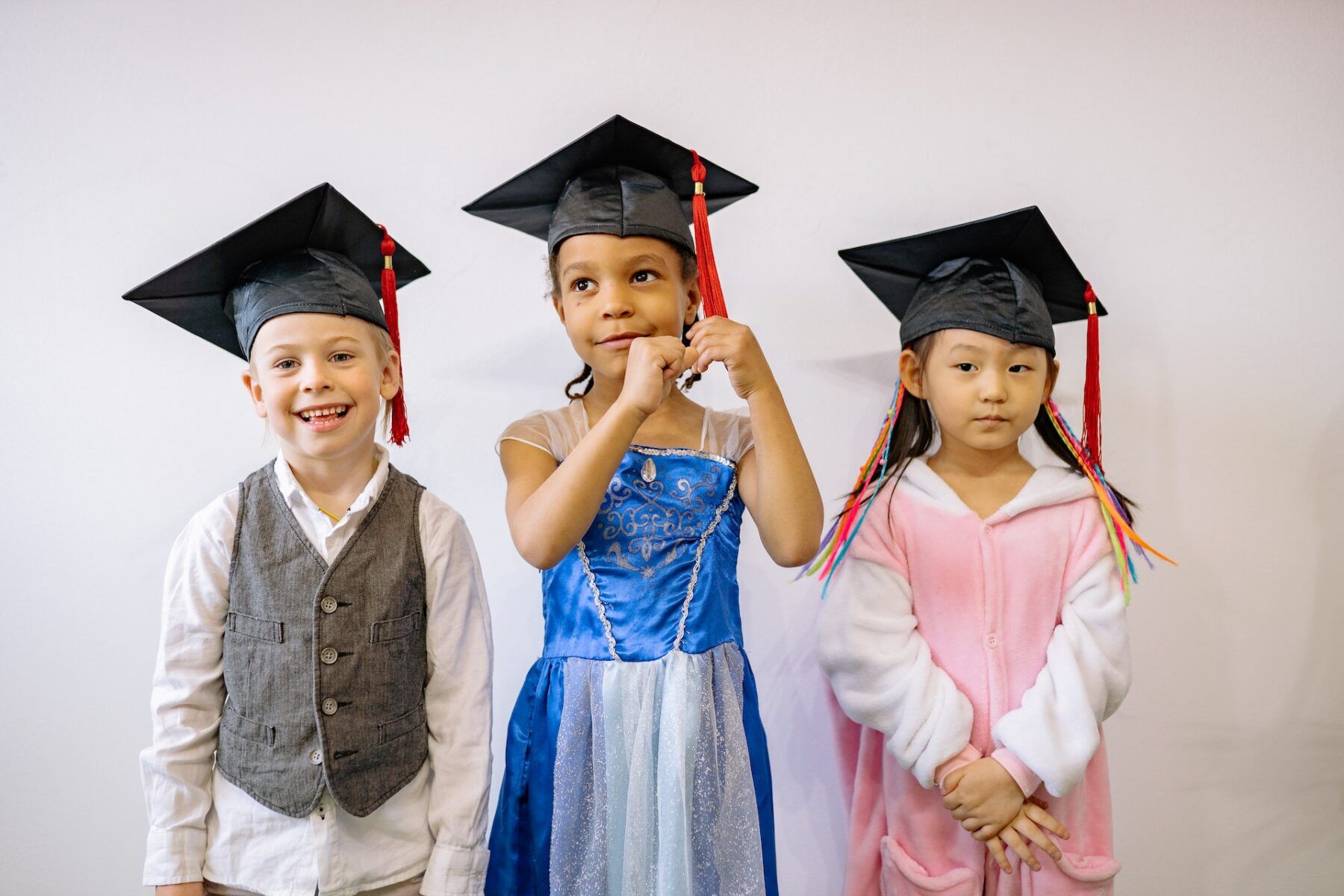 3 kids standing with graduation hats on.