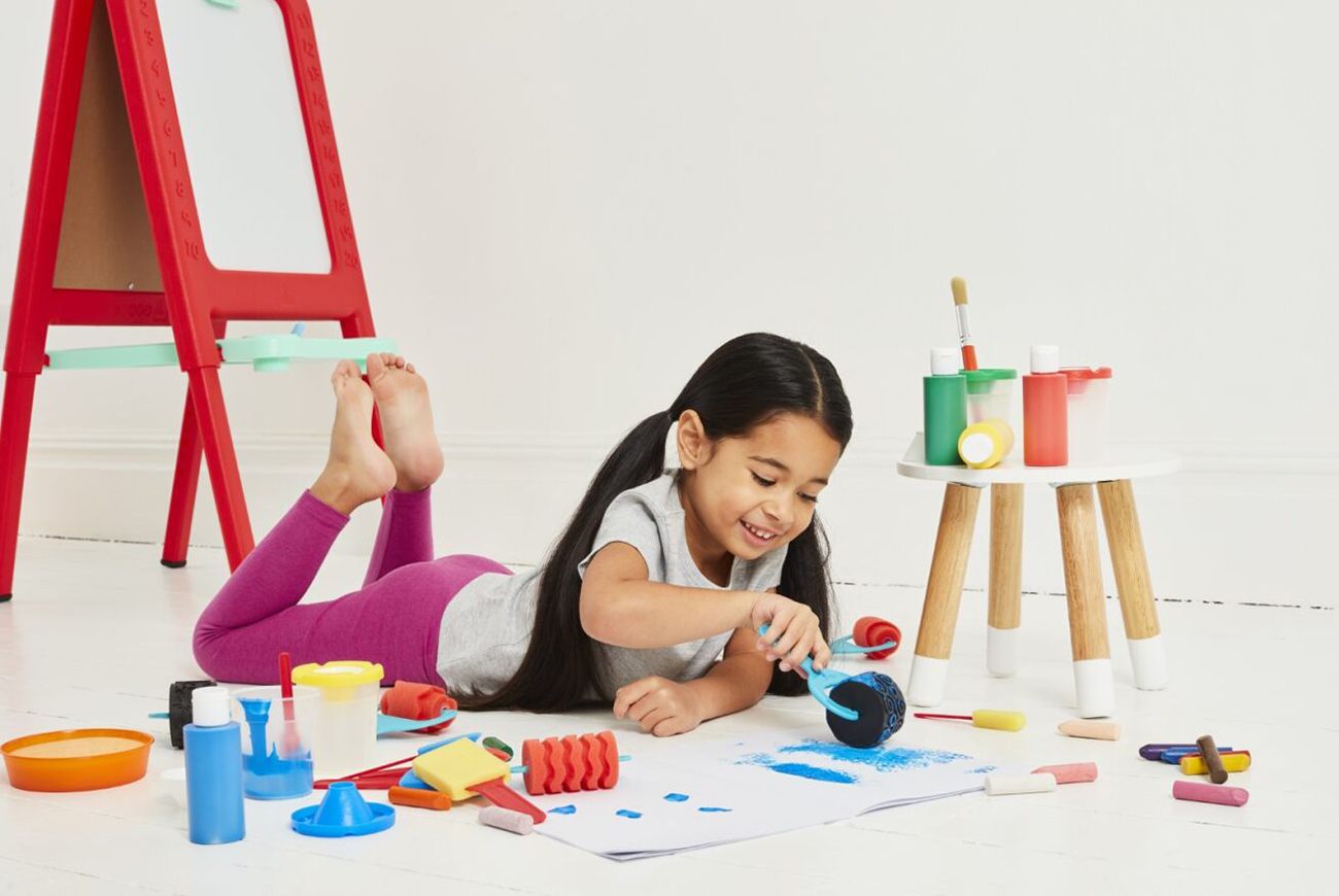 Young girl laying on floor painting with easel in the background