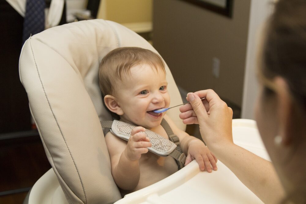 Baby in highchair being fed by mum.