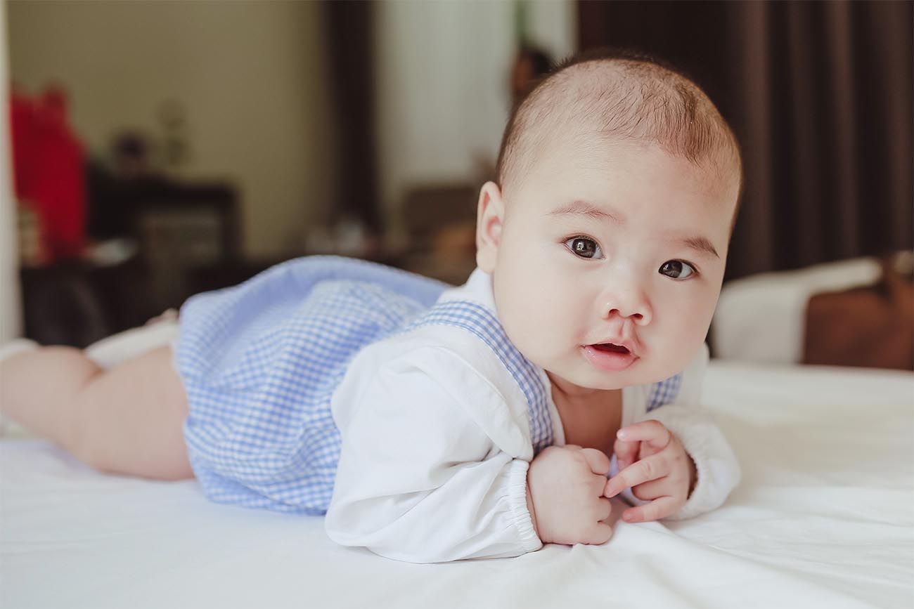 baby on its tummy on a bed looking at the camera