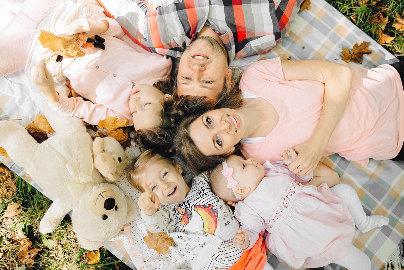 parents with three children lying in a circle on a picnic blanket surrounded by soft toys