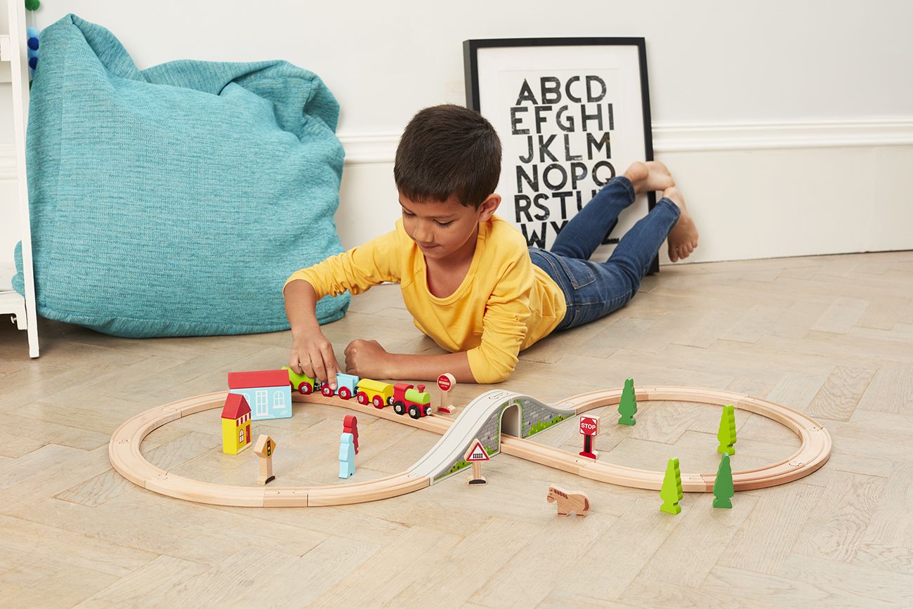 Boy plays with wooden train track.
